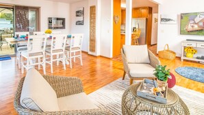 A spacious living area with a dining set, wicker furniture, and a kitchen in the background. - Cornet Bay Cottage in Oak Harbor (Oak Harbor)