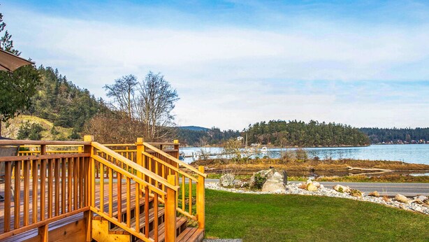 A wooden deck with a railing overlooking a lake and forested hills. - Cornet Bay Cottage in Oak Harbor (Oak Harbor)