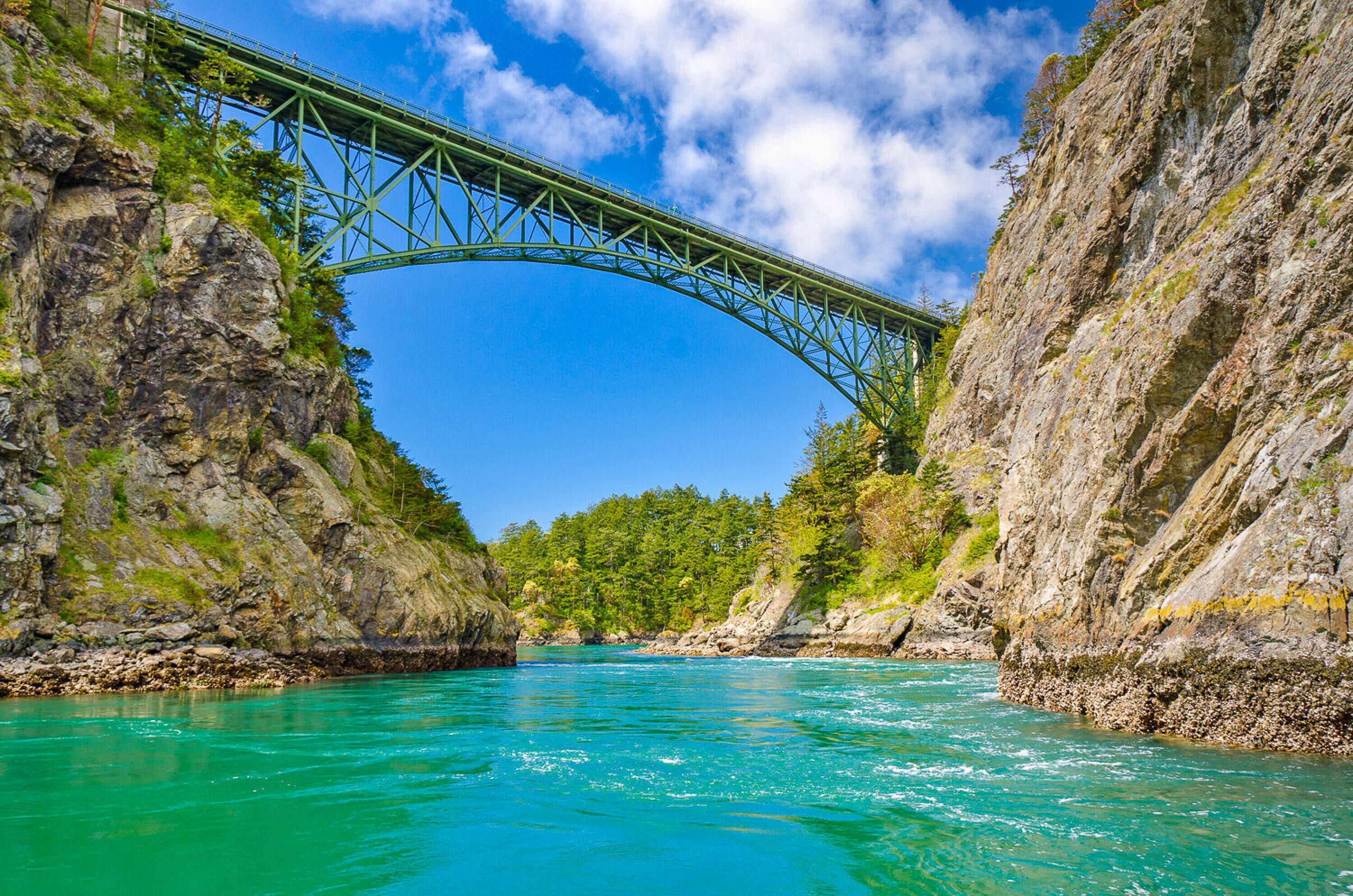 A bridge over a turquoise river with rocky cliffs on either side.
