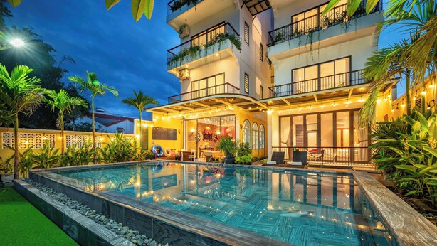 Un hotel con piscina, mobiliario exterior y una entrada bien iluminada.