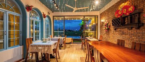 A restaurant with a long wooden table, arched windows, and a brick wall with decorations.