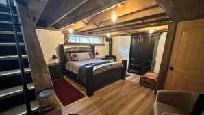 A bedroom with a bed, nightstands, a dresser, a wooden floor, and a staircase. - A Country Stay Just Minutes Away
 (Cambridge)