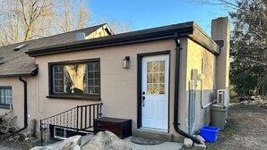 A single-story house with a front porch, a white door, and a small front yard with rocks and a blue trash bin. - A Country Stay Just Minutes Away
 (Cambridge)
