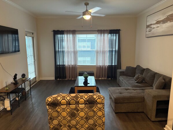 A living room with a sofa, a patterned armchair, a coffee table, and a ceiling fan.
