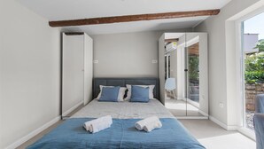 Ein modernes Schlafzimmer mit einem großen Bett, einem Holzbalken an der Decke und Blick ins Freie durch eine Schiebetür.