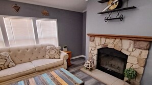 Una sala de estar con chimenea de piedra, un sofá color beige y una mesa de centro colorida.