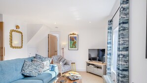 Un salon moderne avec un canapé bleu, des coussins à motifs, une table basse en bois, un téléviseur posé sur un meuble et une grande fenêtre avec des rideaux.