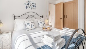 Un lit bien fait, avec du linge de lit blanc et des oreillers à motifs d’étoiles, une table de chevet avec une lampe et une armoire en bois.