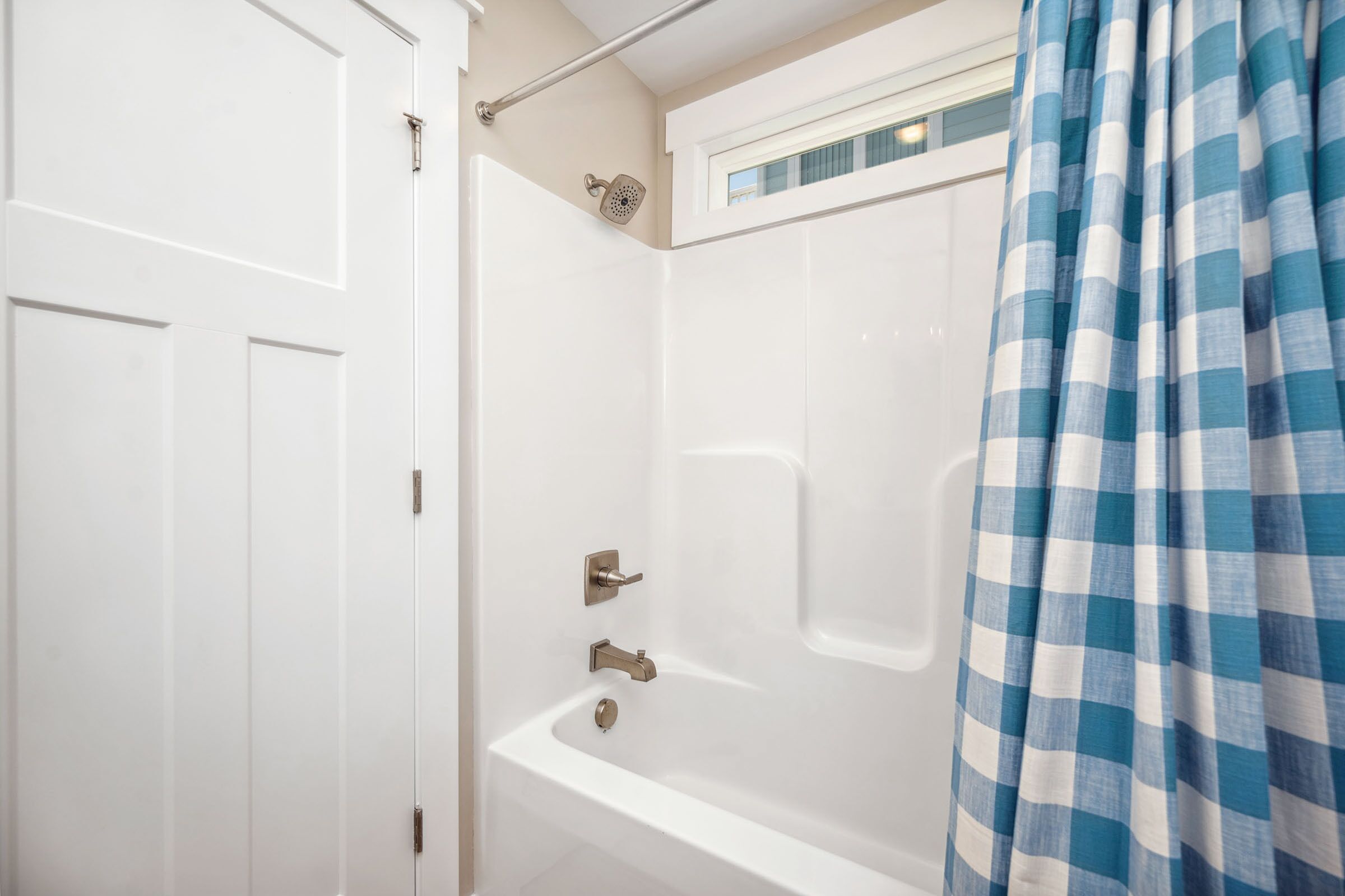 A white bathroom with a shower, a bathtub, and a window above the bathtub.