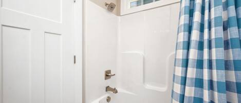 A white bathroom with a shower, a bathtub, and a window above the bathtub.