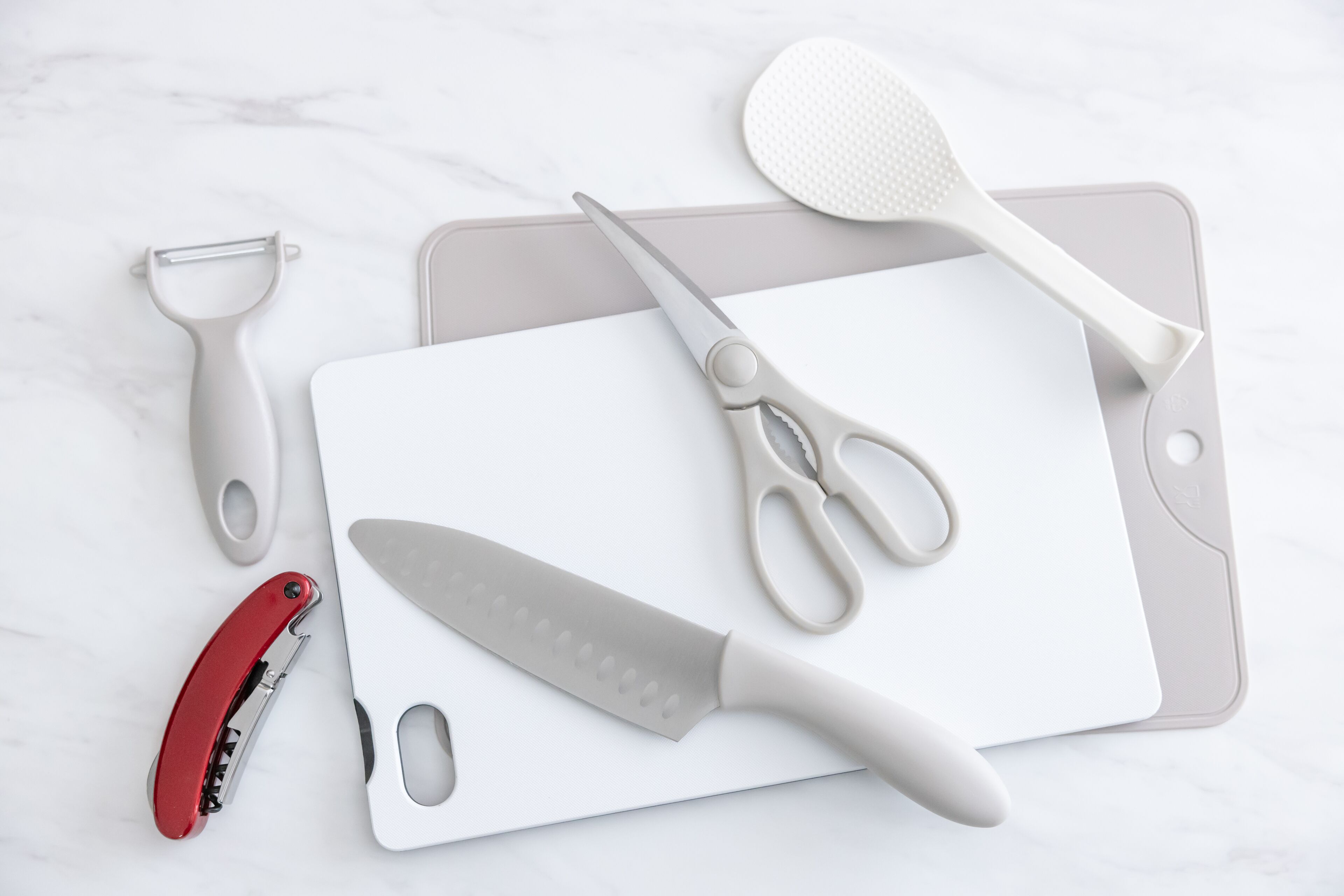 Una encimera de cocina con una tabla de cortar, un cuchillo, un par de tijeras, un rallador y un pelador.