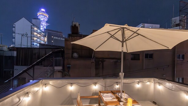 An outdoor dining area with a table set for two, a large umbrella, and string lights. - Tsutenkaku Royal House (Osaka)