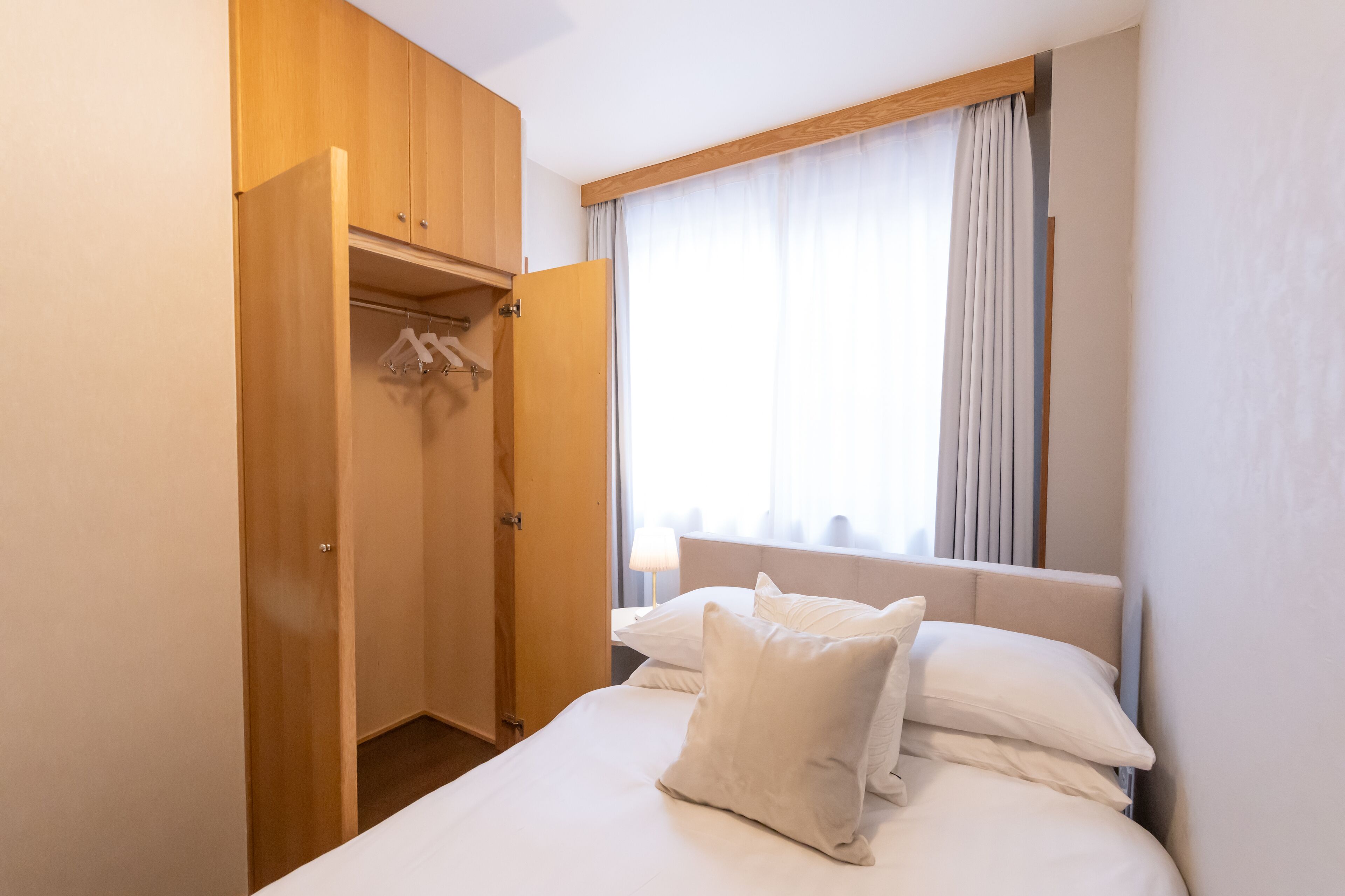 A hotel room with a bed, a wardrobe, and a window with curtains.