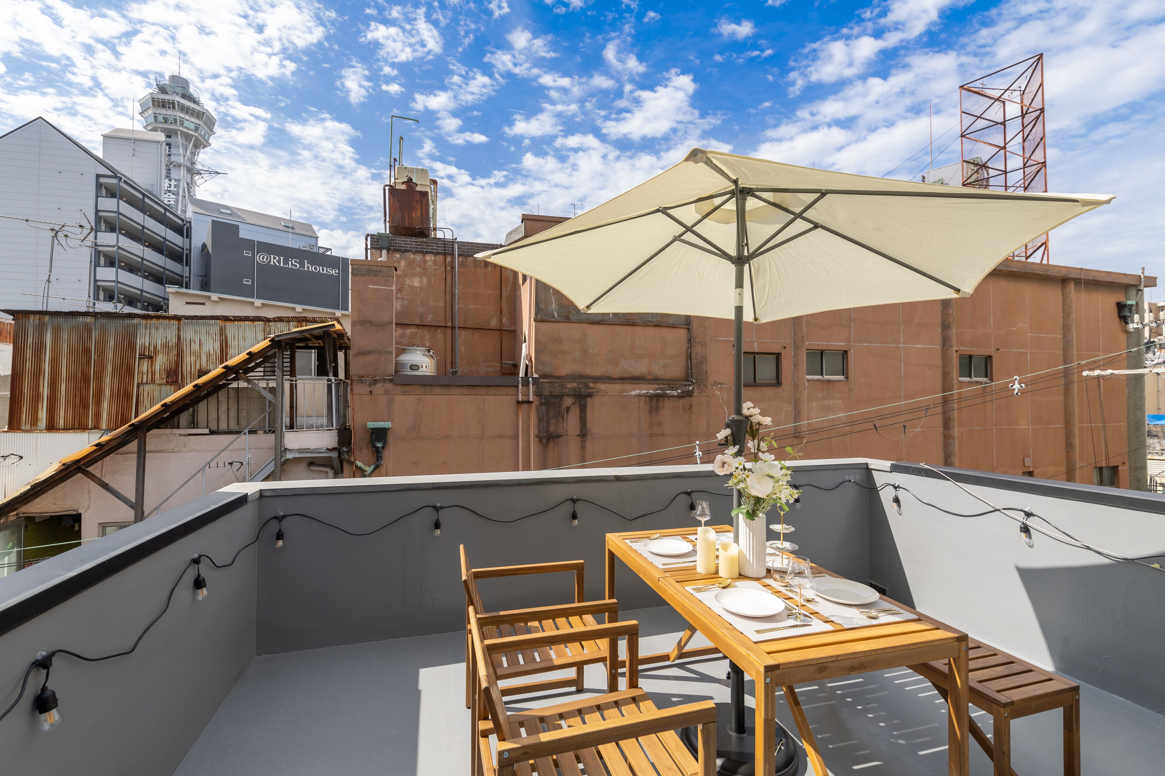 Une terrasse sur le toit, avec une table en bois dressée pour le dîner, un grand parasol et une vue sur le paysage urbain.