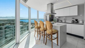 Eine moderne Küche mit Barbereich, großen Fenstern und Blick auf Stadt und Meer.