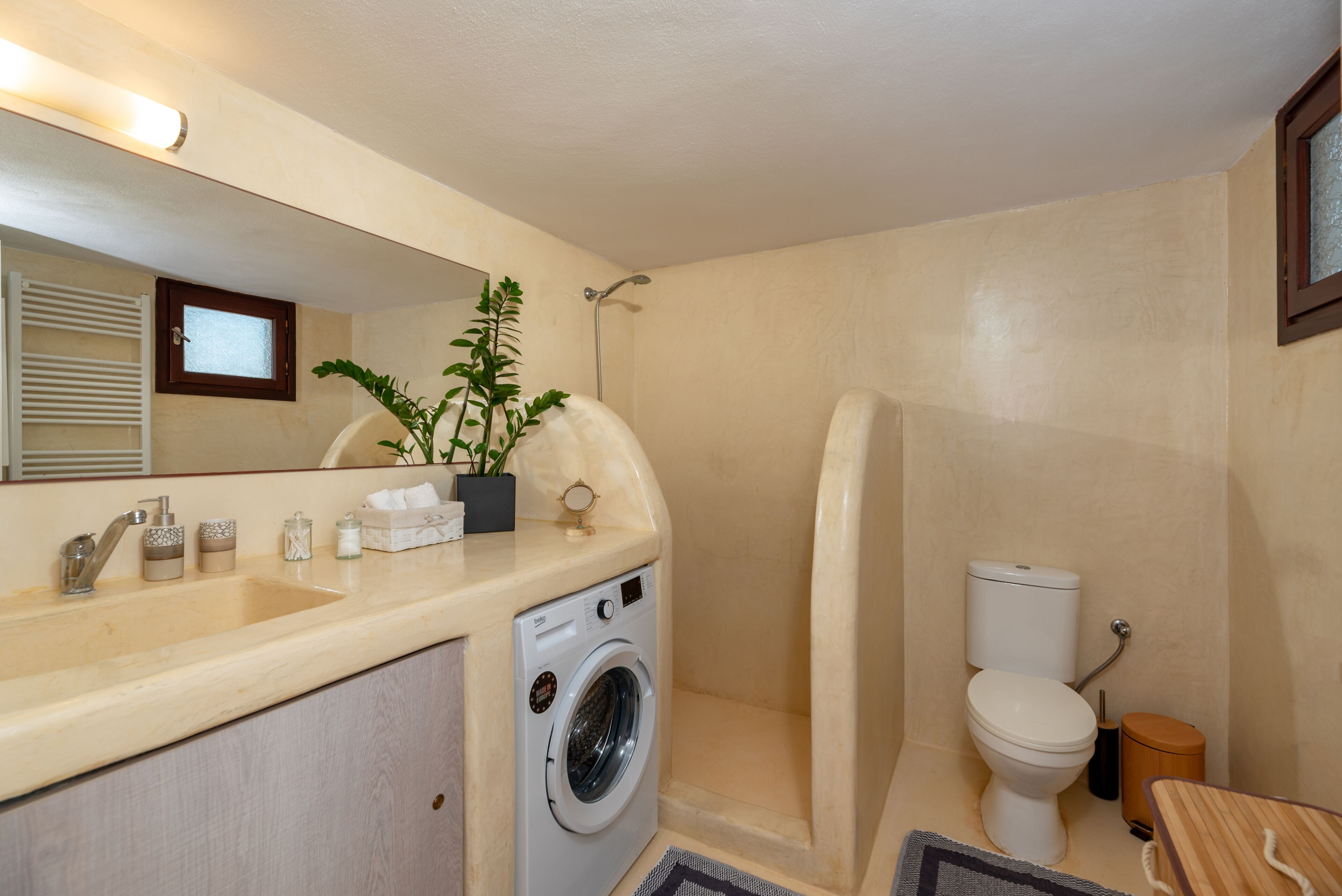 A compact bathroom with a washing machine, toilet, and a small sink.