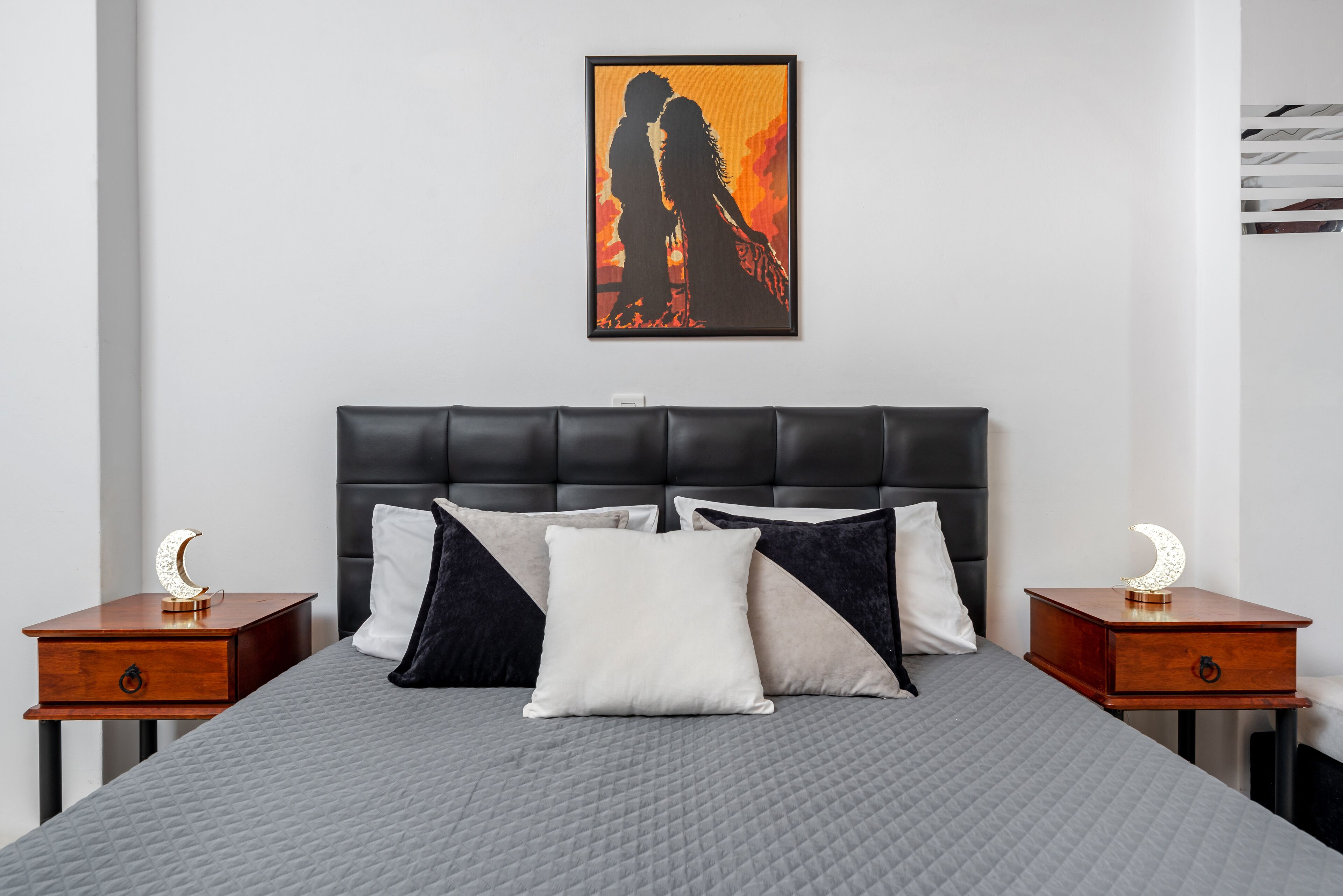 A bedroom with a large bed, two nightstands, a headboard, and a framed picture on the wall.