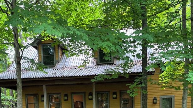 Une maison en bois jaune avec un porche, un chemin menant à l’entrée et un toit en métal.