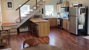 Une cuisine moderne avec un plancher en bois, un réfrigérateur en acier inoxydable et un escalier en bois menant à un coin repas.