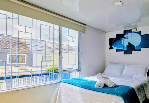 A hotel room with a large window, a bed with white bedding, and a wall art piece. - Charming Family Retreat in the Heart of Bogotá (Bogotá)