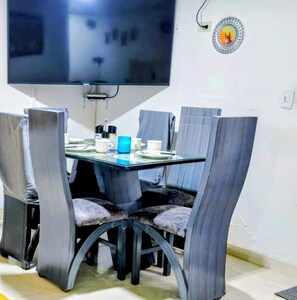 A dining area with a glass table, four chairs, and a television mounted on the wall. - Charming Family Retreat in the Heart of Bogotá (Bogotá)