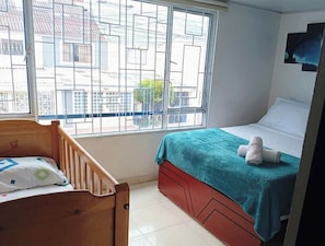A bedroom with a single bed, a wooden crib, and a window with a view of buildings. - Charming Family Retreat in the Heart of Bogotá (Bogotá)