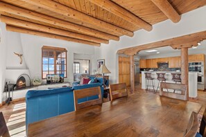 Un salón espacioso con un sofá azul, vigas de techo de madera y una chimenea.