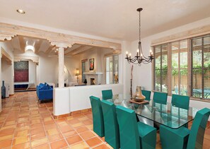 A dining area with a glass table and teal chairs, a fireplace, and a view through large windows.