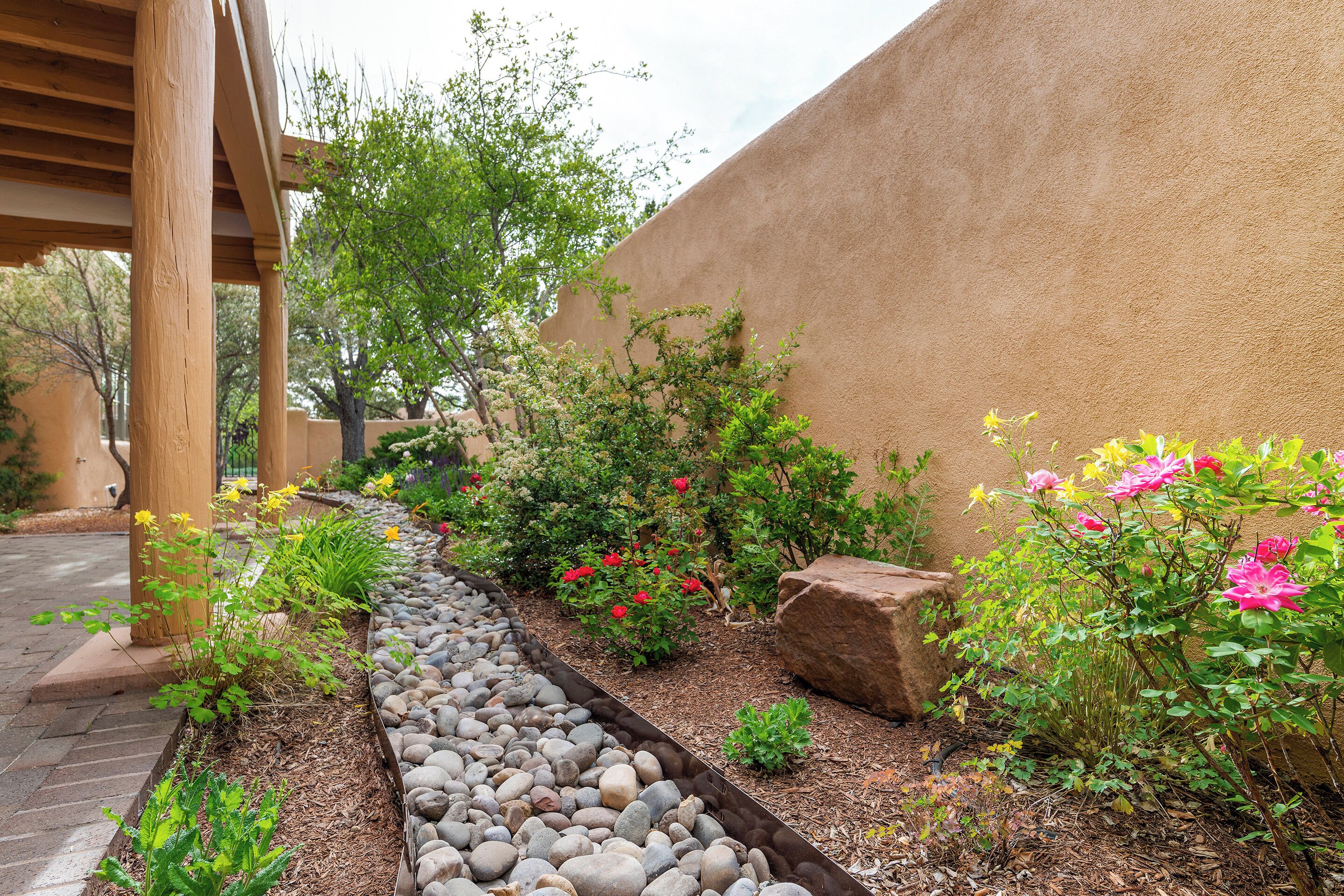 Un jardin avec un chemin en pierre, différentes plantes et une structure de pergola en bois.