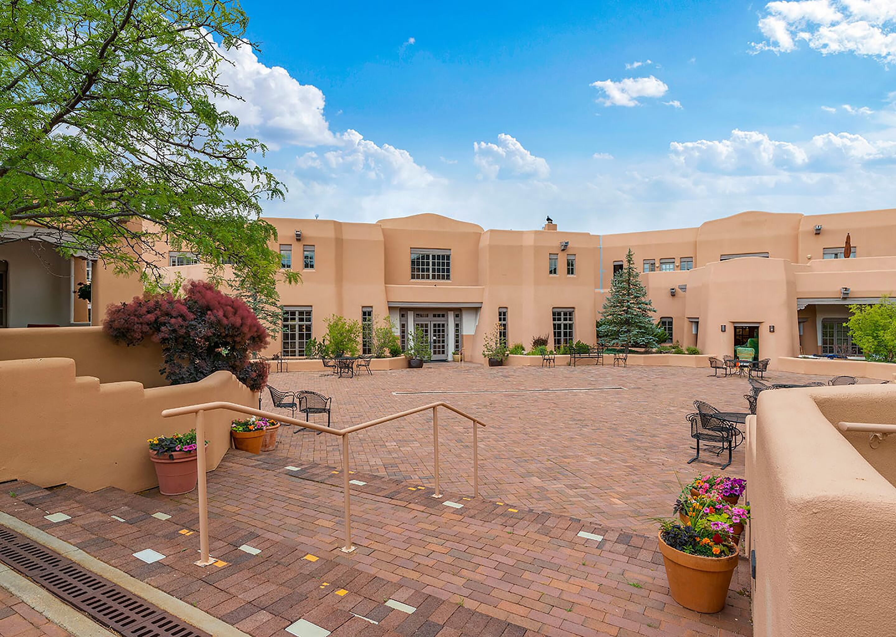 A courtyard with a brick pathway, outdoor seating, and a building with multiple windows and doors.