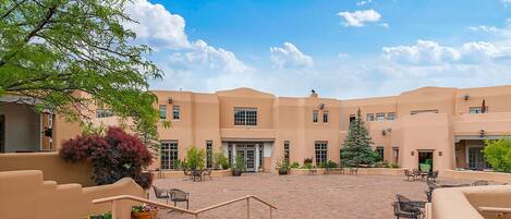 A courtyard with a brick pathway, outdoor seating, and a building with multiple windows and doors.