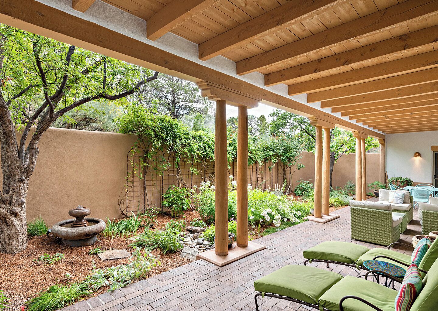 A covered patio with a brick floor, green cushioned seating, and a pergola structure.