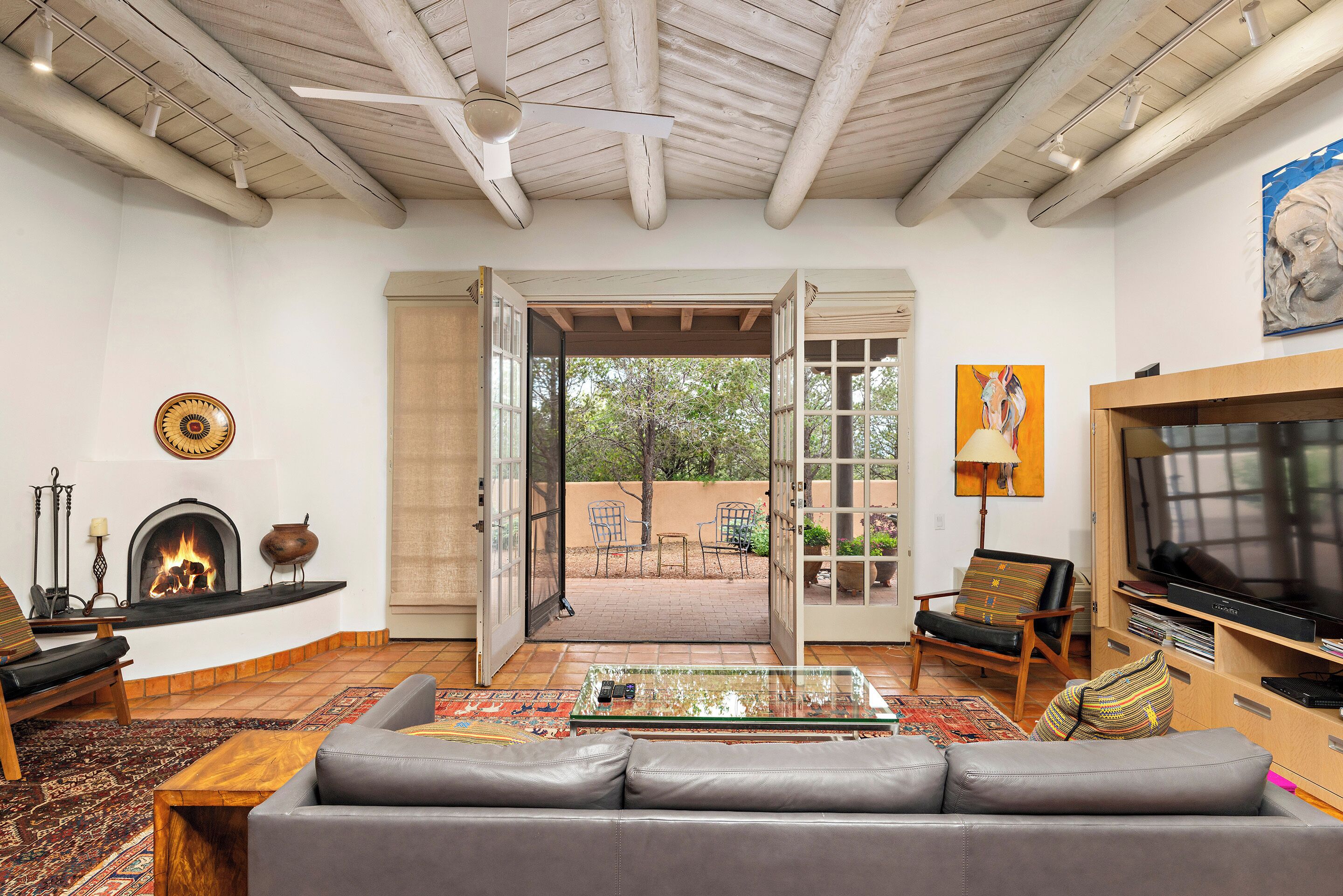 A living room with a fireplace, sofa, television, and an open door leading to an outdoor patio.
