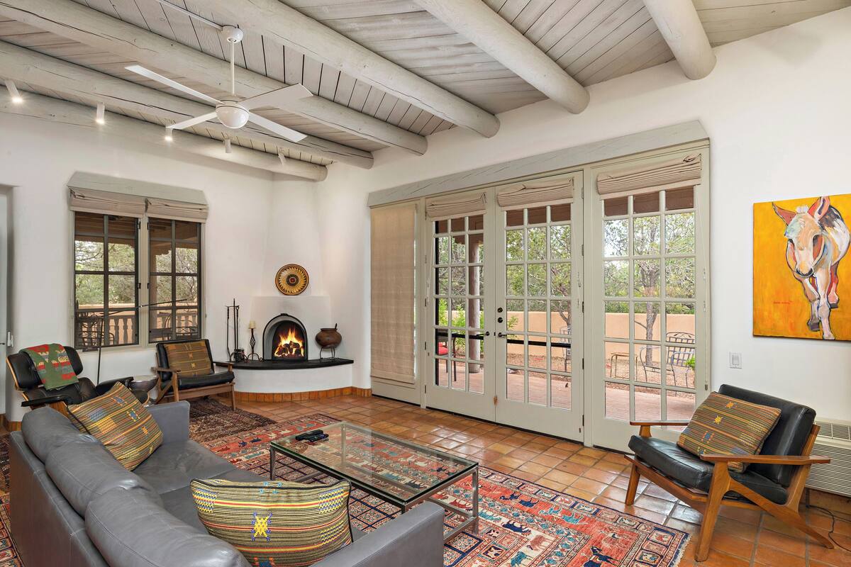 A living room with a sofa, chairs, a fireplace, a glass coffee table, and a large window with a view.
