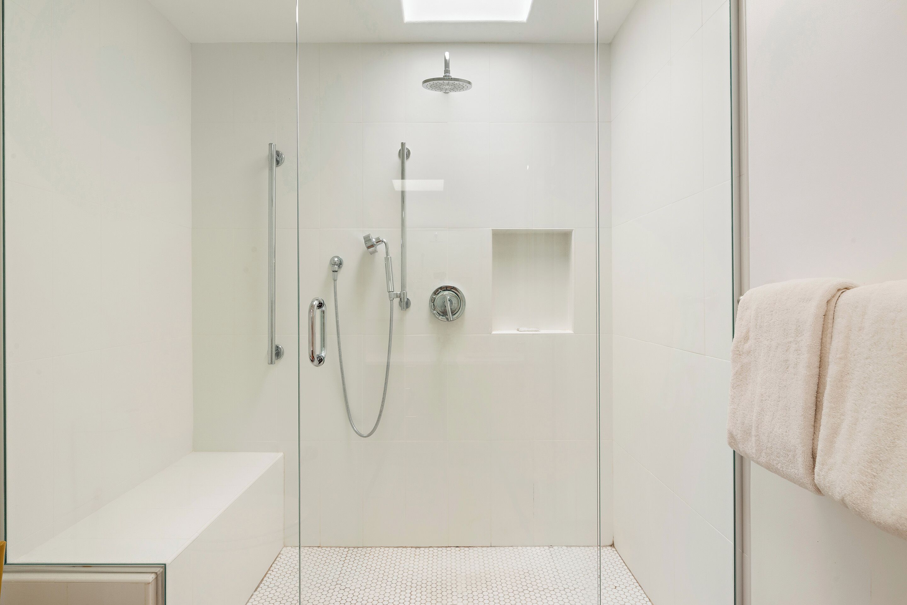 A glass-enclosed shower with a handheld showerhead, a wall-mounted faucet, and a control panel.