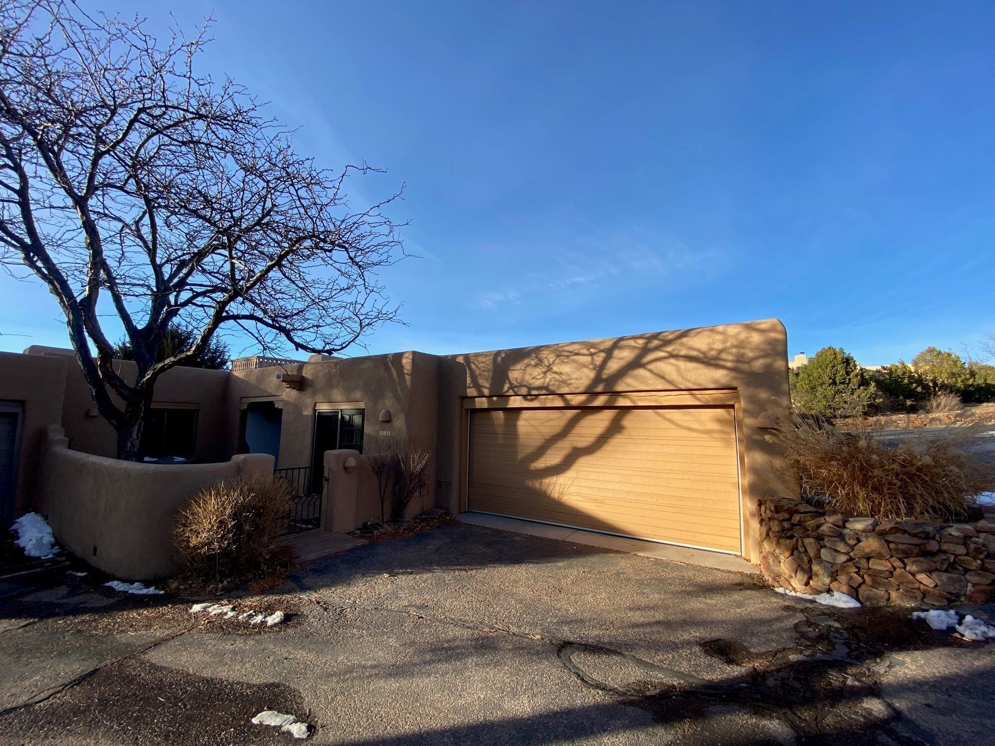 A single-story building with a garage, a tree, and a stone wall.