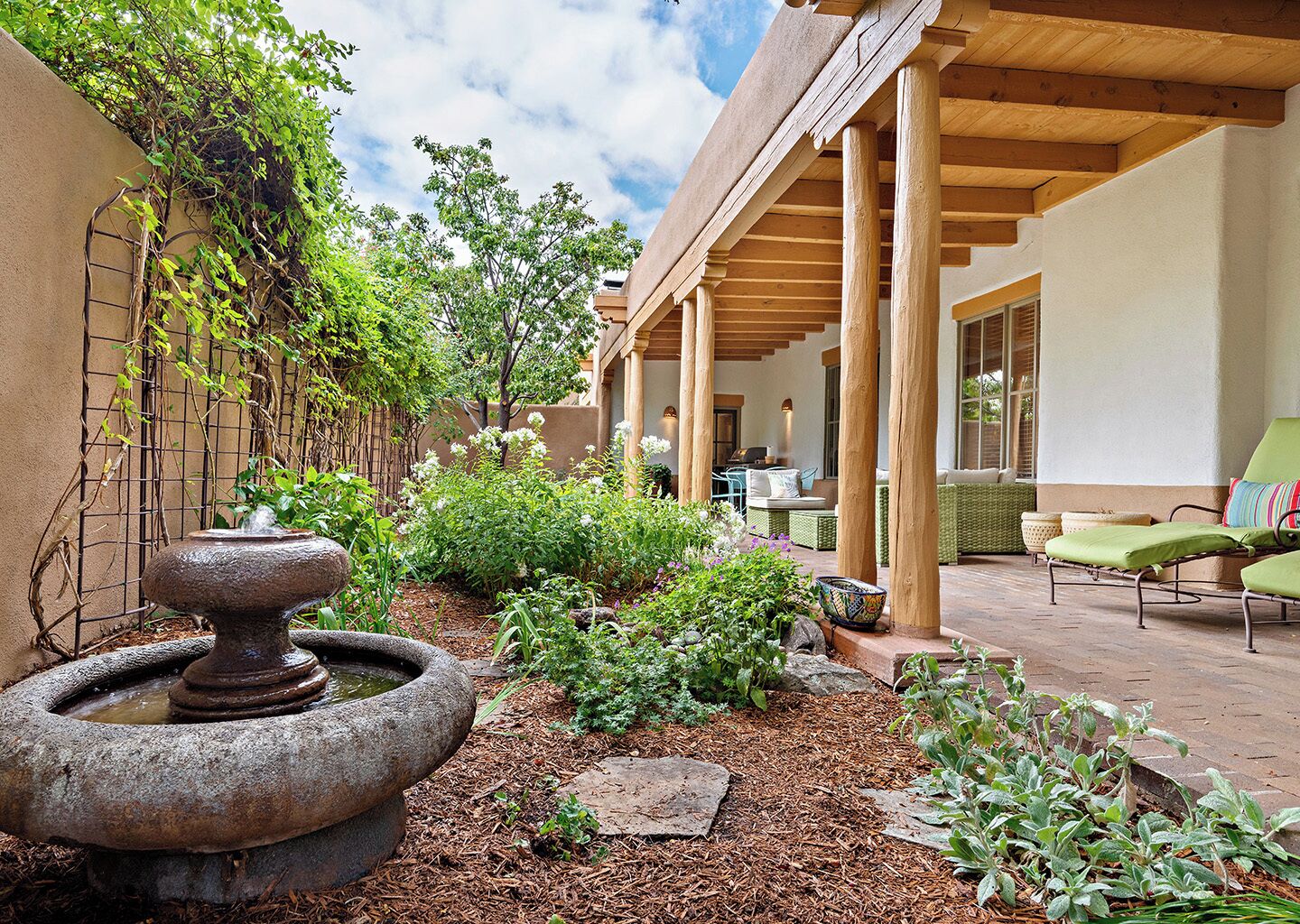 A covered outdoor patio with a stone fountain, lush greenery, and seating areas.