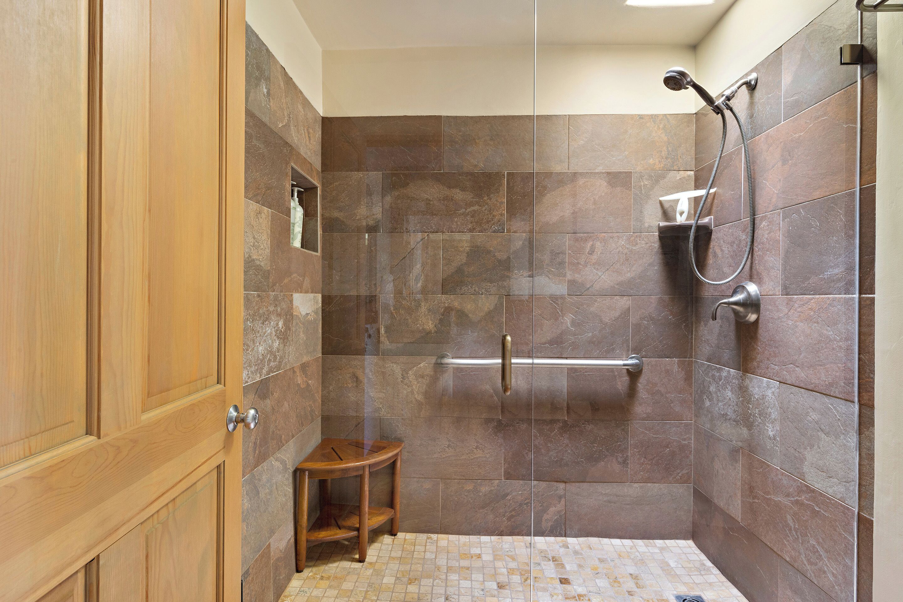 Un área de ducha con puerta de cristal, un taburete de madera y un perchero para toallas.