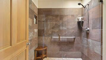 A shower area with a glass door, a wooden stool, and a towel rack.