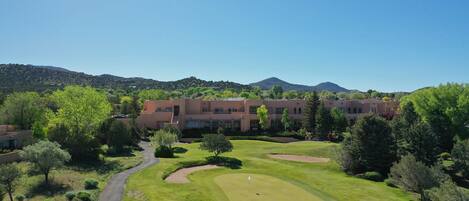 A golf course with bunkers, a putting green, and a building in the background.