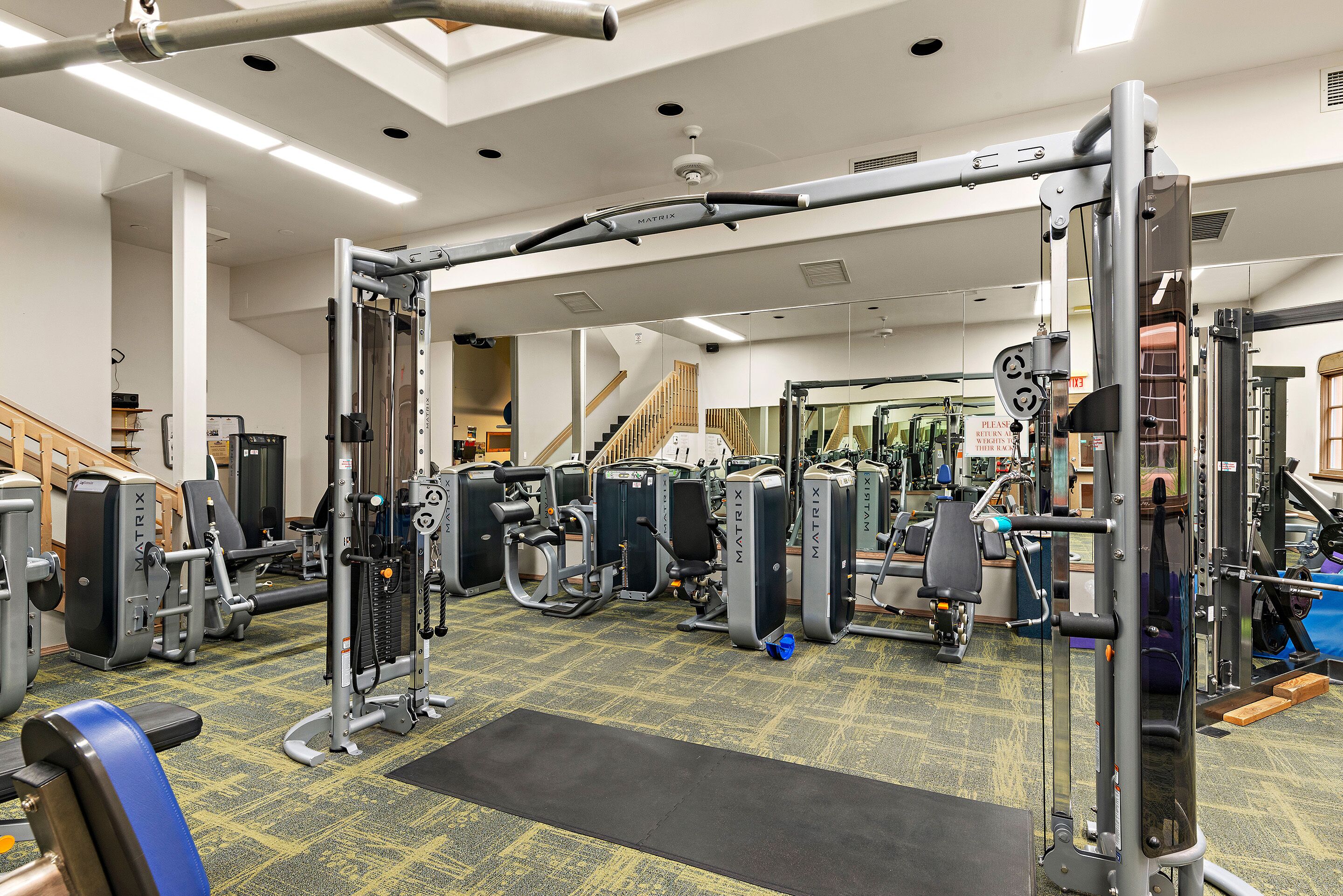 Ein Fitnessstudio mit verschiedenen Trainingsgeräten, einer Treppe und einem Spiegel.