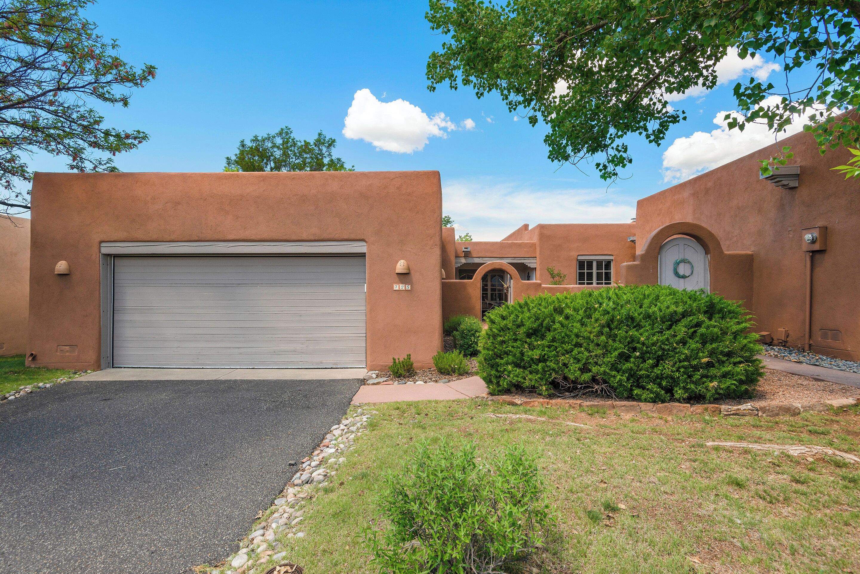 A stucco building with a closed garage door, a small front yard with a bush, and a clear blue sky.
