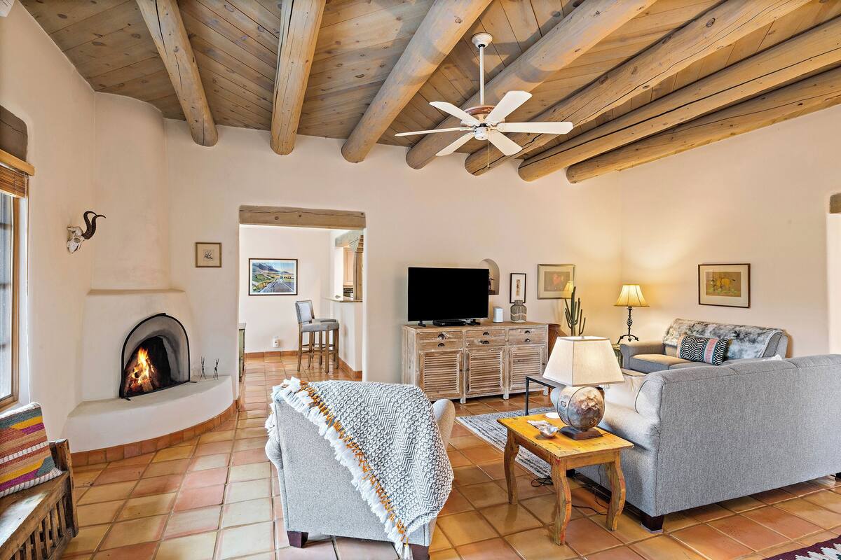 A cozy living room with a fireplace, a ceiling fan, a sofa, a TV, and a dining area.