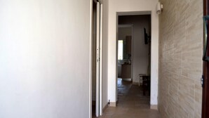 Un couloir étroit, dont le sol est recouvert de carreaux, mène à une cuisine avec une fenêtre.