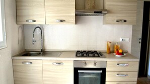 Une cuisine moderne avec des meubles de couleur bois clair, un évier en acier inoxydable, une cuisinière à gaz et un four encastré.