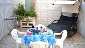 Une terrasse avec une table dressée pour un repas, entourée de chaises, d’un fauteuil inclinable et d’un étendoir.