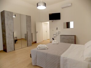 Un dormitorio moderno con cama, armario, televisor y espejo.