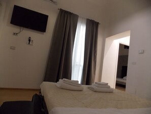A hotel room with a bed, a TV mounted on the wall, and a window with curtains. - Mammarusina (Brindisi)