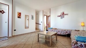 A room with a wooden table, a sofa with floral upholstery, a mirror, and a staircase leading to another level. - Casa Vacanze Orlando - Con Veranda Vista Mare A 200 M Dal Mare (Castrignano del Capo)