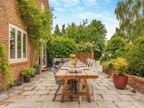 A patio with a wooden table set for dining, surrounded by potted plants and a brick wall. - Perfect for family and friends get togethers to enjoy coast and countryside. (Walpole St Peter, near King&rsquo;s Lynn)